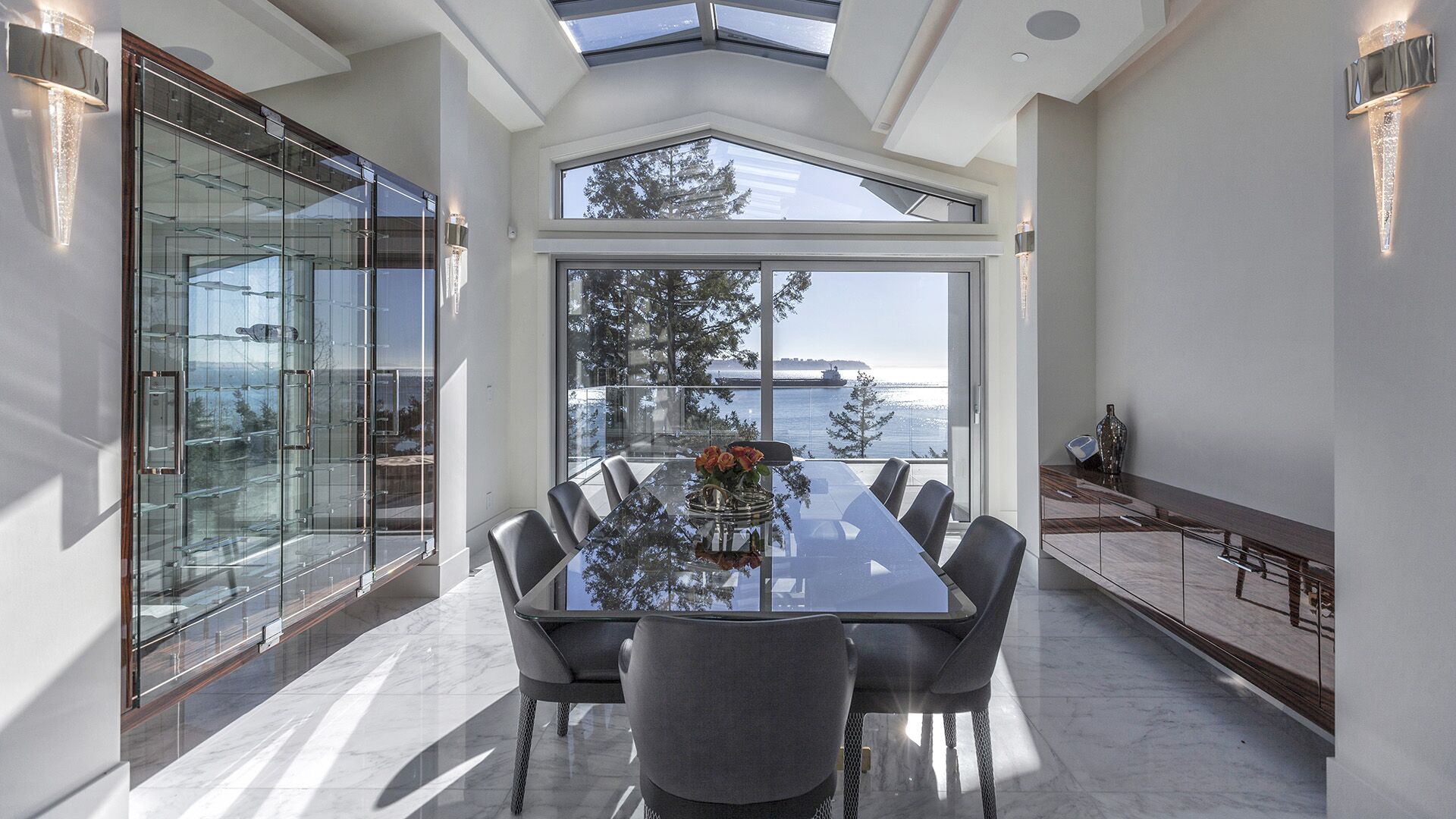Formal dining room with glass wine display cabinet crystal wall sconces peak window ocean views and zebrawood credenza at The Riva Club designed and installed by Eurohouse Construction