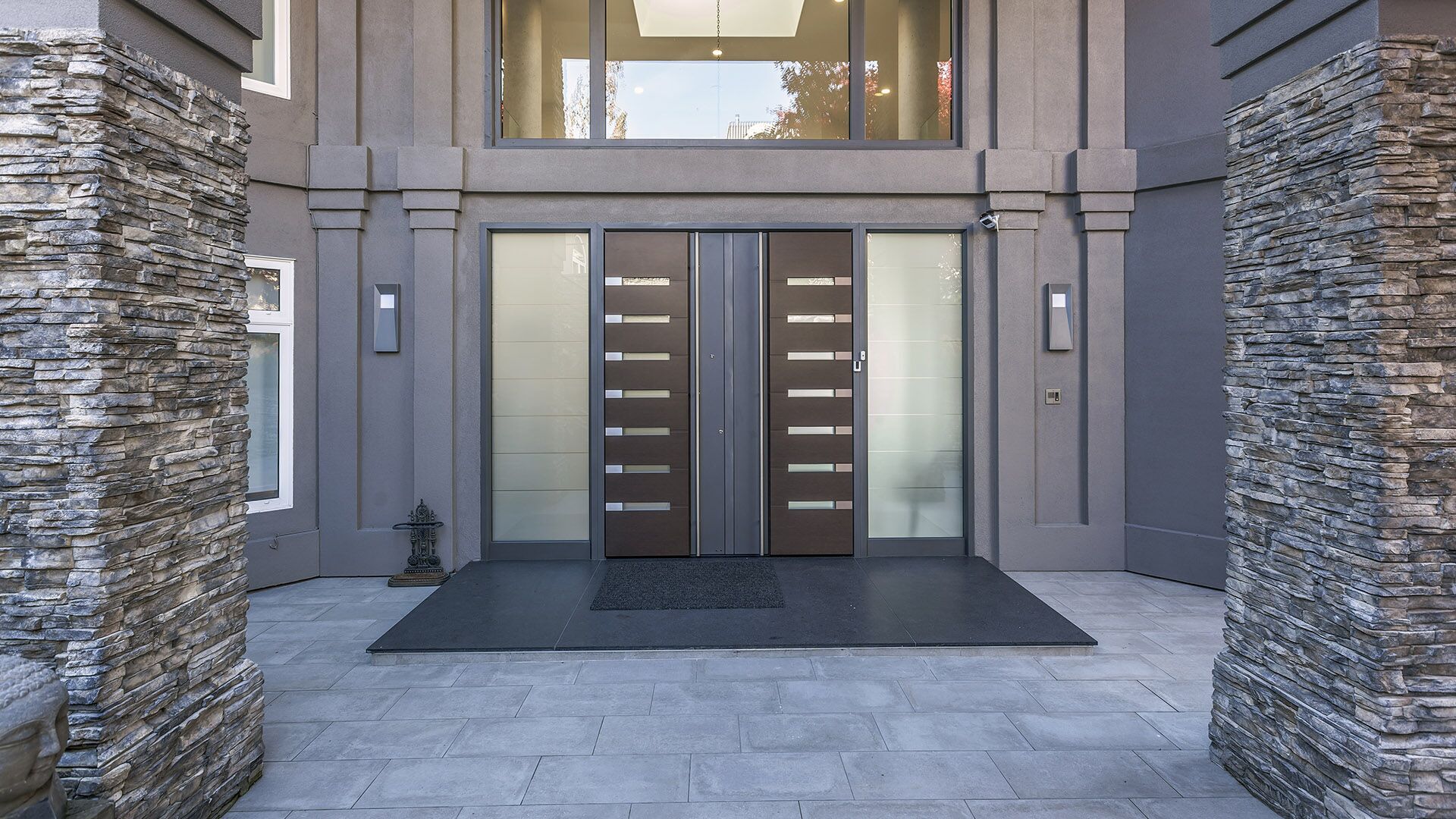 Exterior front entrance with stacked natural stone columns new porcelain stone paving Italian entry door and stucco facade after building envelope remediation at The Zen on Bramwell renovated by Eurohouse Construction