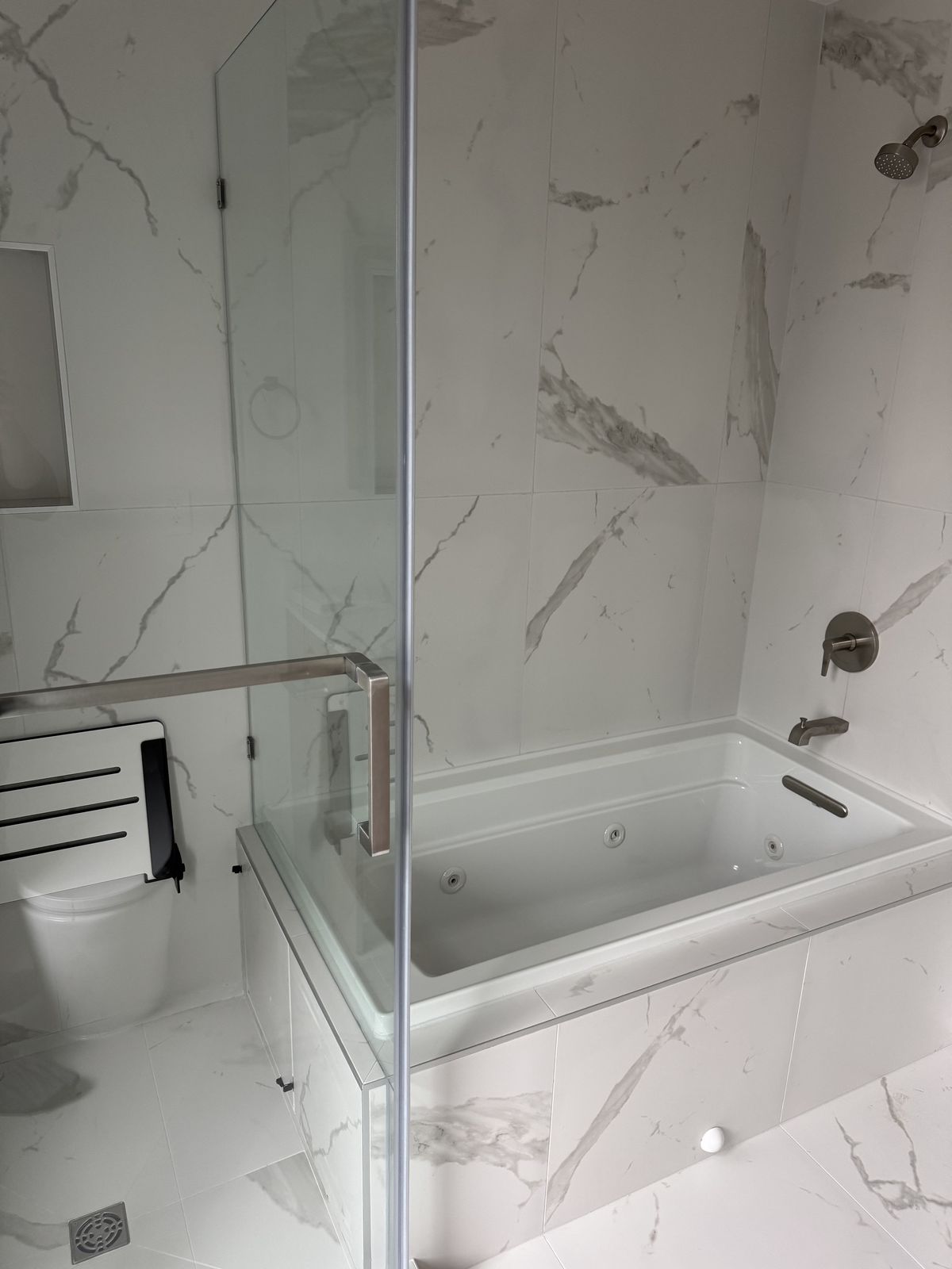 Bathroom with full marble tile, soaker tub, and frameless glass enclosure — fire damage restoration Vancouver
