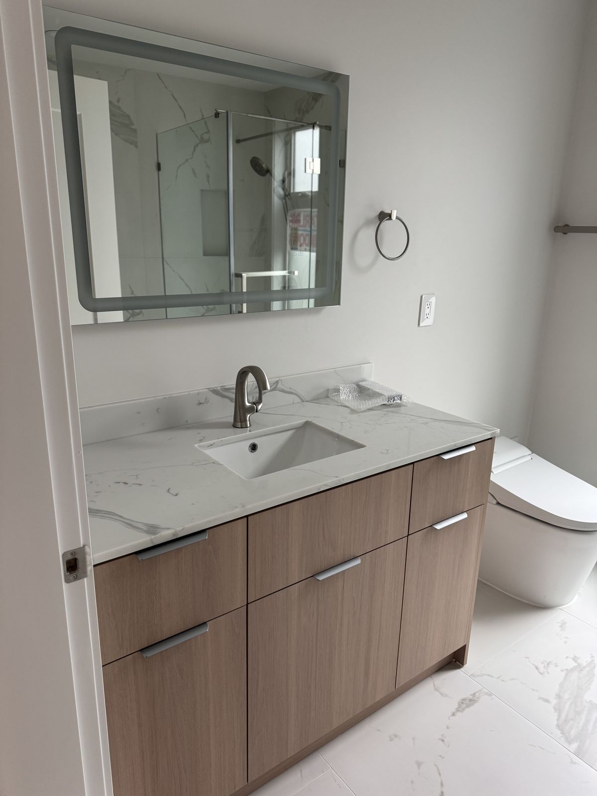 Bathroom vanity with walnut cabinet, marble countertop, and backlit mirror — insurance restoration finishing