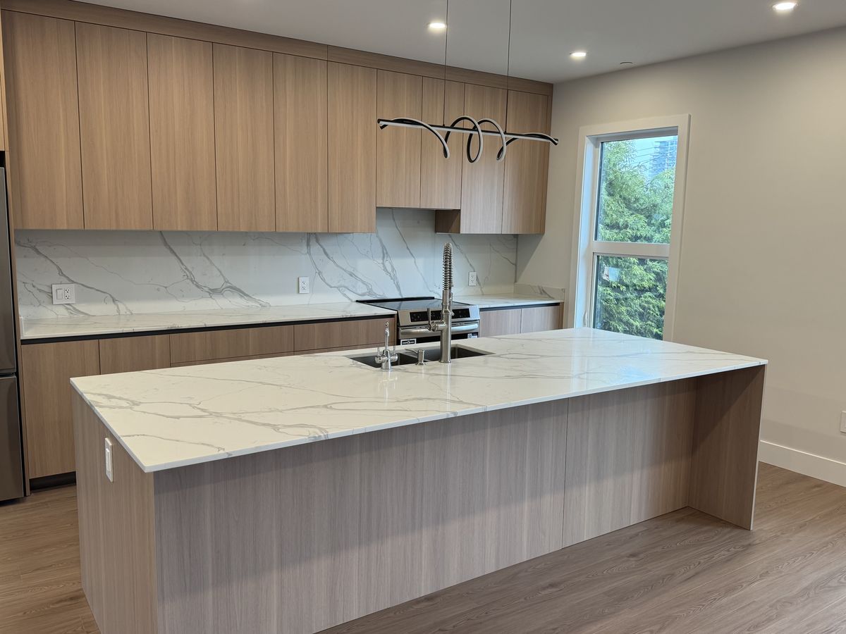 Completed kitchen with marble island countertop, walnut cabinetry, and modern pendant light — fire restoration rebuild Vancouver