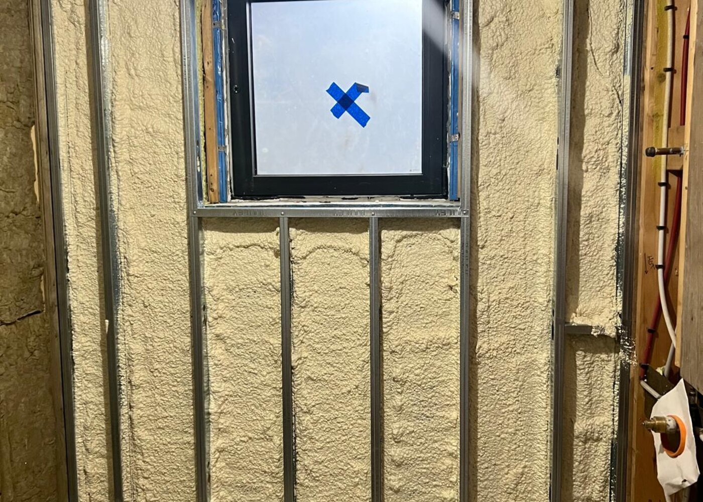 Basement wall with spray foam insulation, steel stud framing, and new window installed during reconstruction