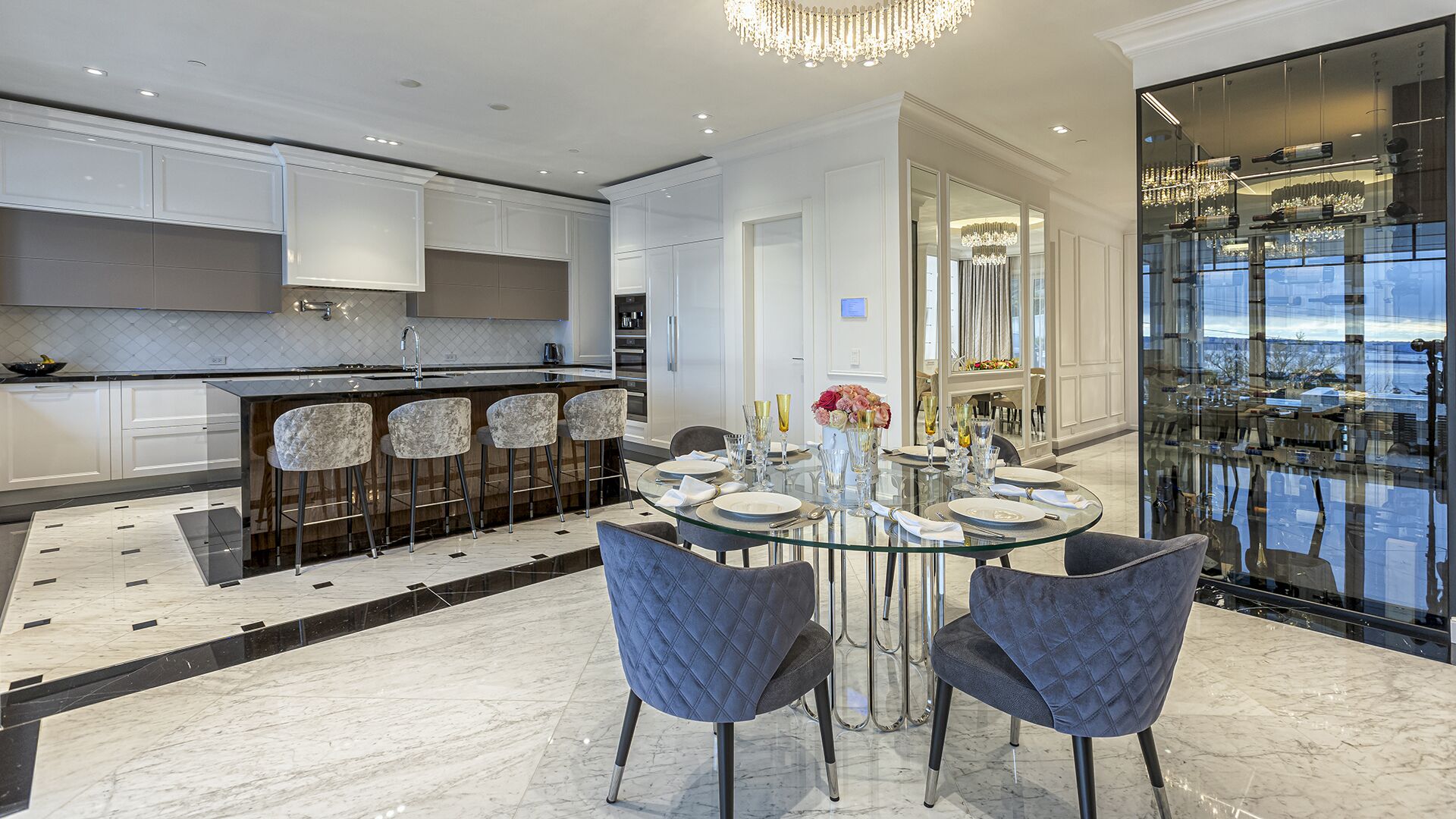 Chef kitchen wide view with dark stone island velvet bar stools marble floors wine display and crystal chandelier luxury West Vancouver home by Eurohouse